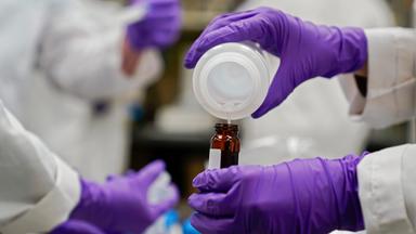 Mehre Hände in lila Handschuhen mixen Chemikalien