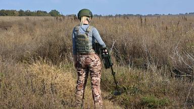 Eine Frau sucht mit einem Metalldetektor nach Minen im Boden - in der Ukraine keine Seltenheit. Immer mehr Frauen werden zu Minensucherinnen ausgebildet.