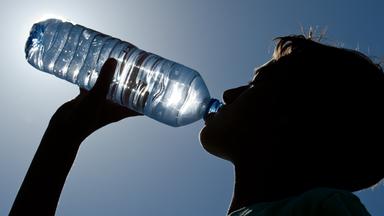 Um sich etwas Abzukülung zu zu verschaffen, trinkt eine Mann aus einer Wasserflasche