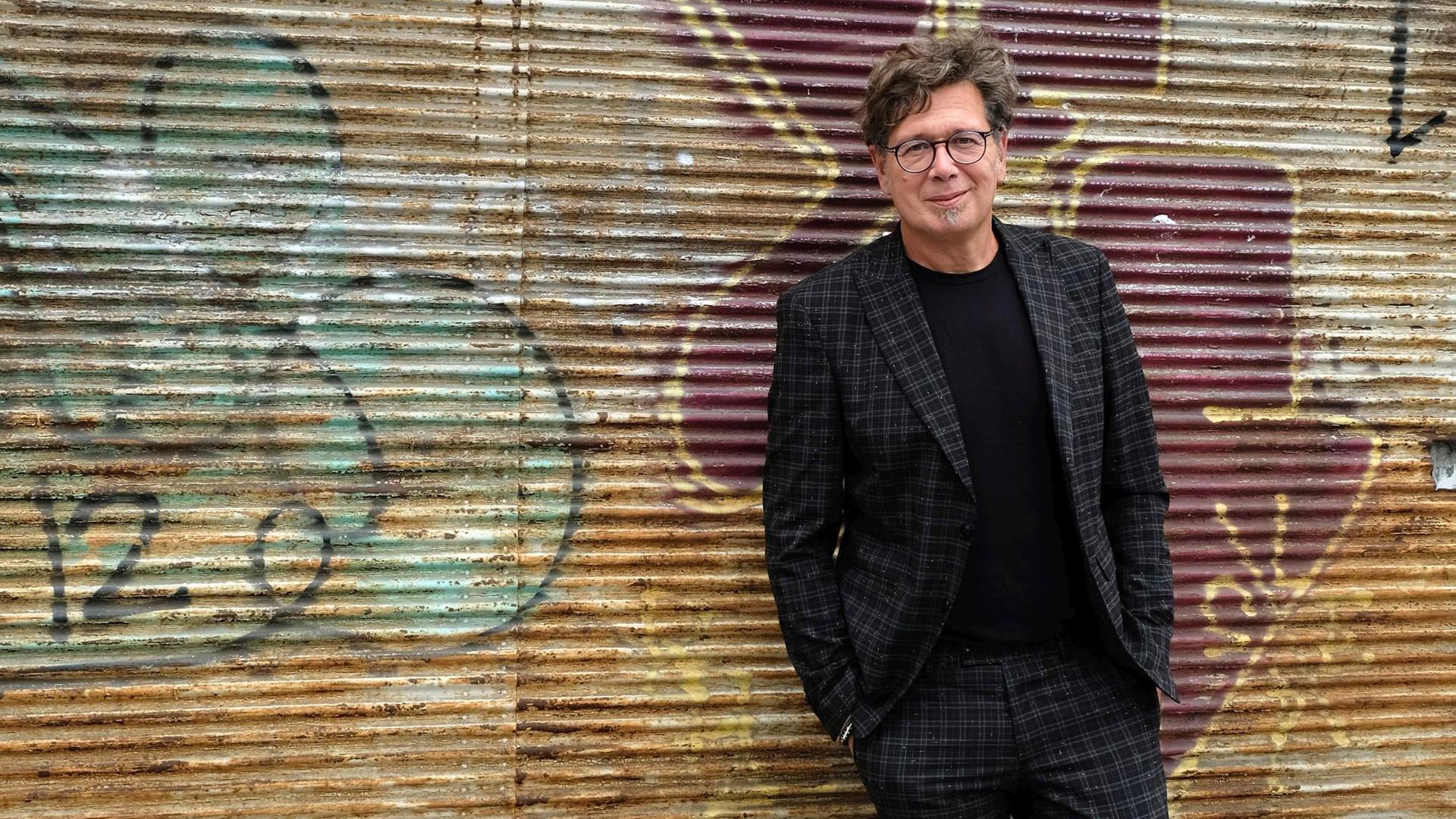 Österreichischer Schriftsteller Franzobel im schwarz gemusterten Anzug vor mit Graffiti versehener Wand.