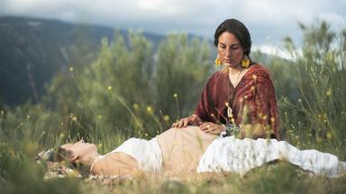 Zwei Welten in mir": Eine Frau liegt im Gras, ihr Schwangerschaftsbauch ist nackt. Tiziana kniet daneben und gibt ihr eine Bauchmassage. - 37°Leben.