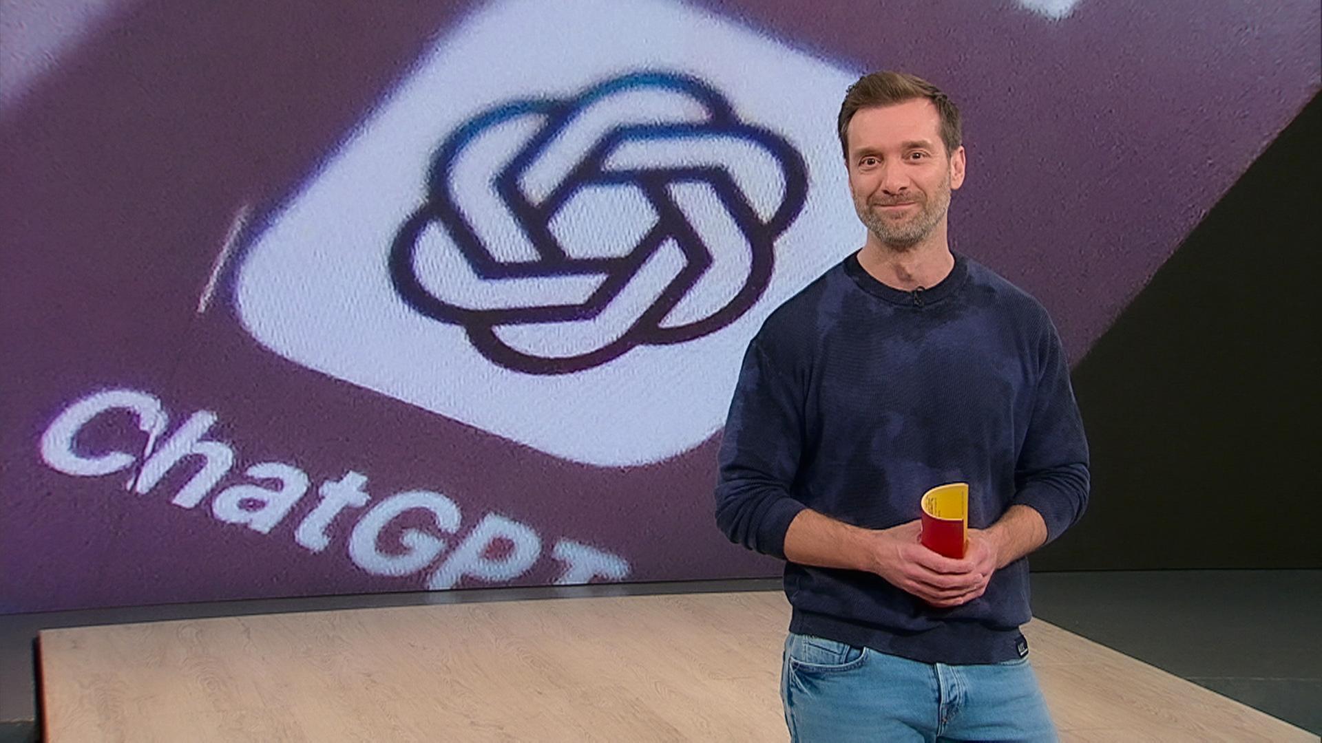 Moderator steht lächelnd im Servicezeit-Studio. Im Hintergrund sieht man das App-Logo der der KI "ChatGPT".