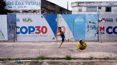 Junge spielt Ball vor COP30-Schild