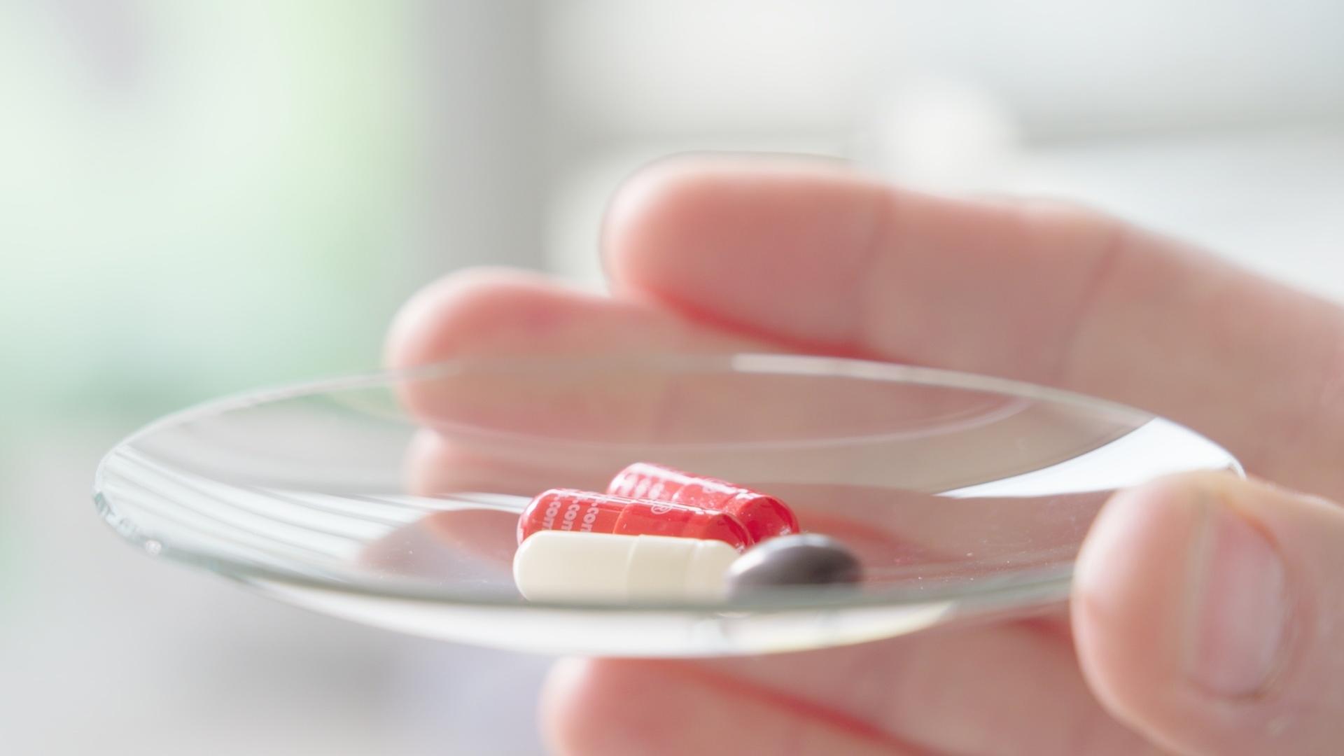 Placebos können zum Schmerzen lindern. Bild: Eine Hand hält einen Teller mit Pillen.