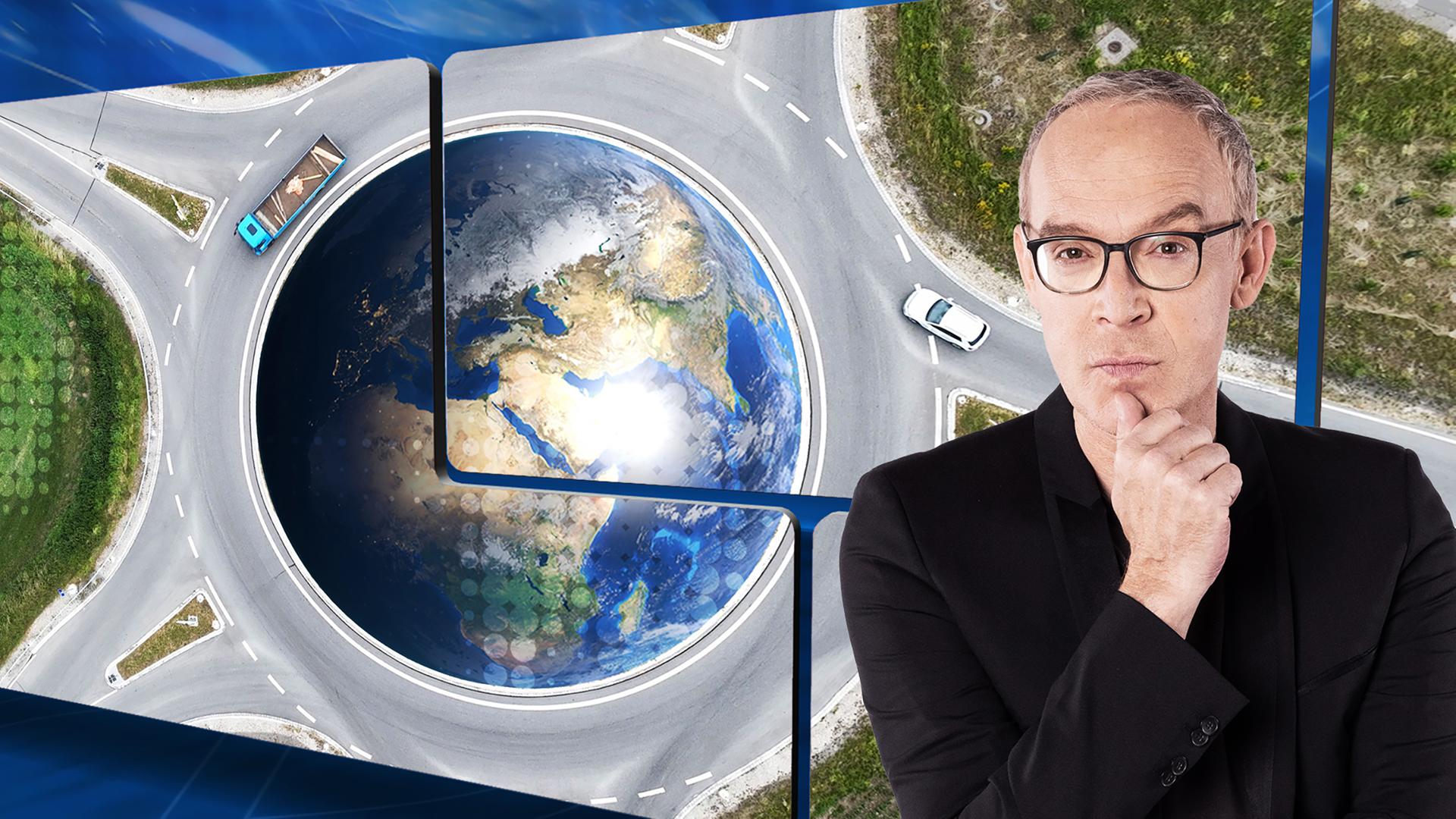 Der Moderator vor einer Videowand, auf der ein Verkehrskreisel und Autos zu sehen sind. In der Mitte eine Weltkugel.