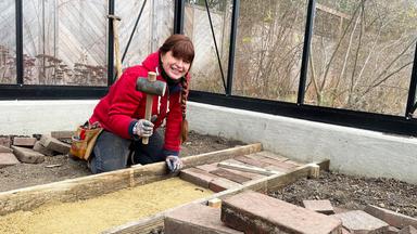 Gartenexpertin Sabrina Nitsche legt im Querbeet-Garten im Gewächshaus einen Weg an.