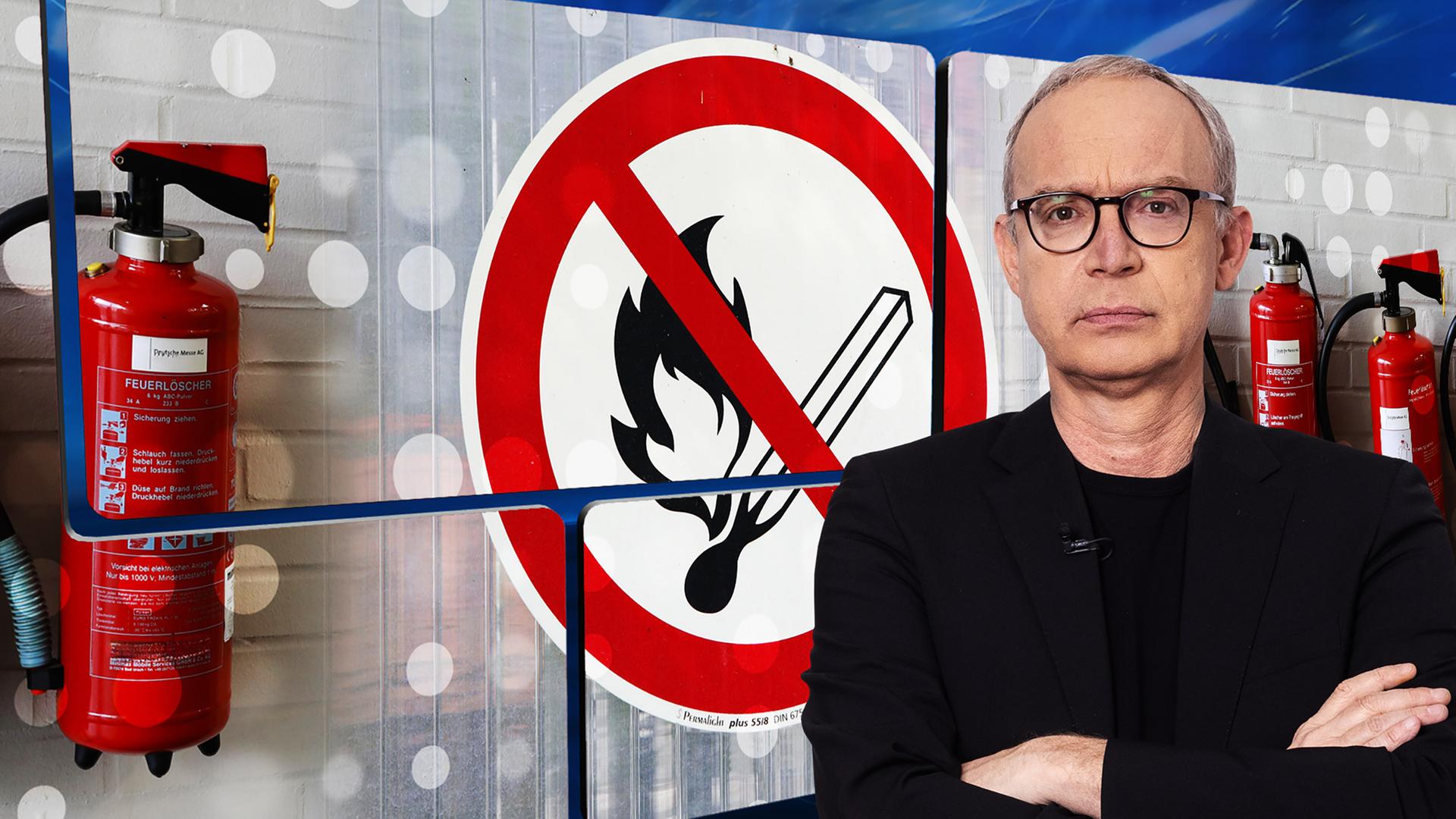 Der Moderator mit ernstem Gesicht vor einer Videowand, auf der Feuerlöscher zu sehen sind und ein Schild mit einem durchgestrichenen brennenden Streichholz.
