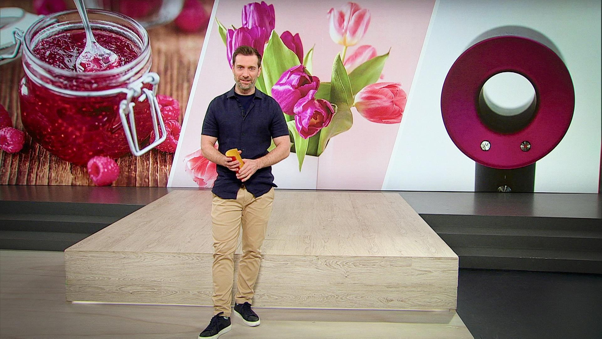 Ein junger Mann steht im Studio vor einem Hintergrundbild mit Konfitüre, Schnittblumen und einem Föhn