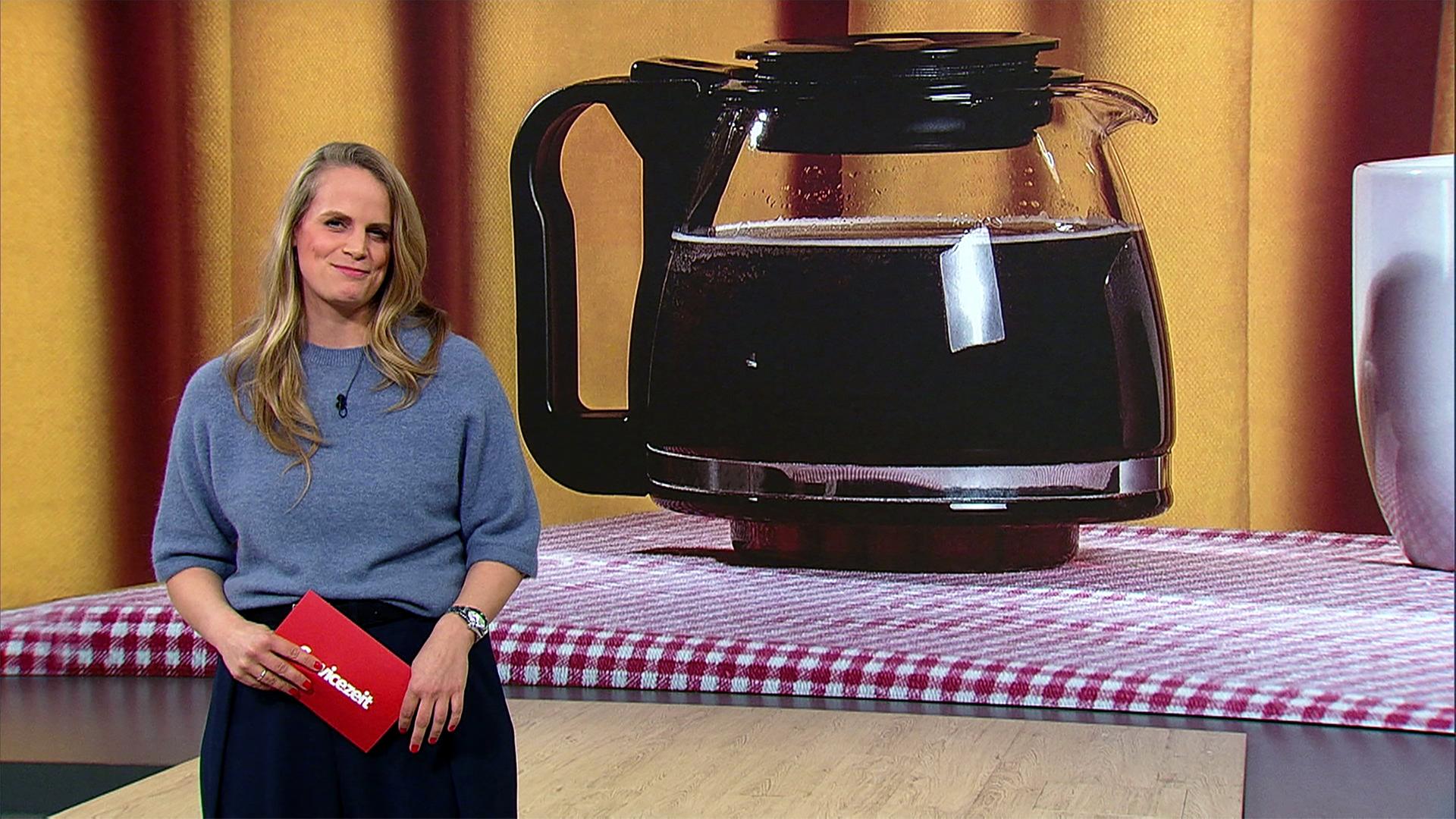 Eine junge Frau steht im Studio vor einem Hintergrundbild mit einer Kanne Filterkaffee