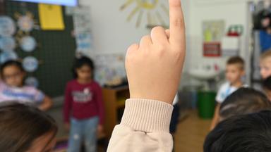 Lehrermangelctrifft Schüler an Schulen in benachteiligter Lage besonders. Was muss sich ändern? (Bild zeigt Unterricht im Klassenzimmer, im Vordergrund ein nach oben gestreckter Arm)