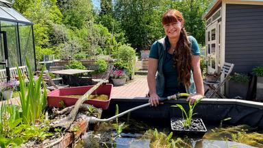 Sabrina Nitsche (Moderatorin) mit einem Gartenschlauch in der Hand vor dem Hochbeet-Mini-Teich.