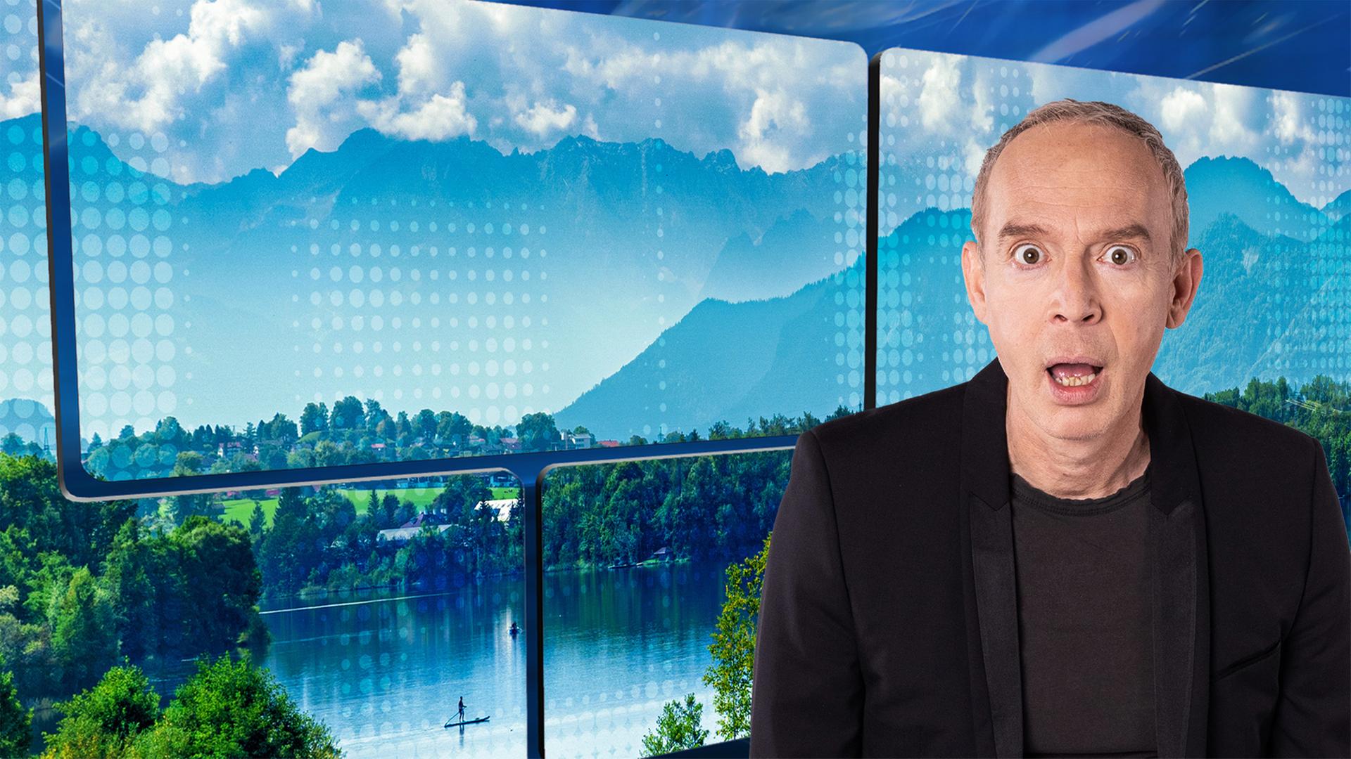 Christoph Süß steht mit fragendem Gesichtsausdruck vor einem Hintergrund mit wolkigem, blauem Himmel, Bergen und einem See als Motiv.