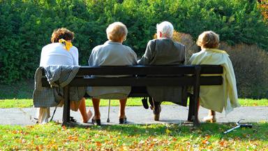 Vier Senioren sitzen an einem sonnigen Herbsttag auf einer Parkbank