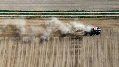 bayern: ein landwirt wirbelt mit seinem traktor beim bearbeiten eines feldes staub auf (luftaufnahme mit drohne)