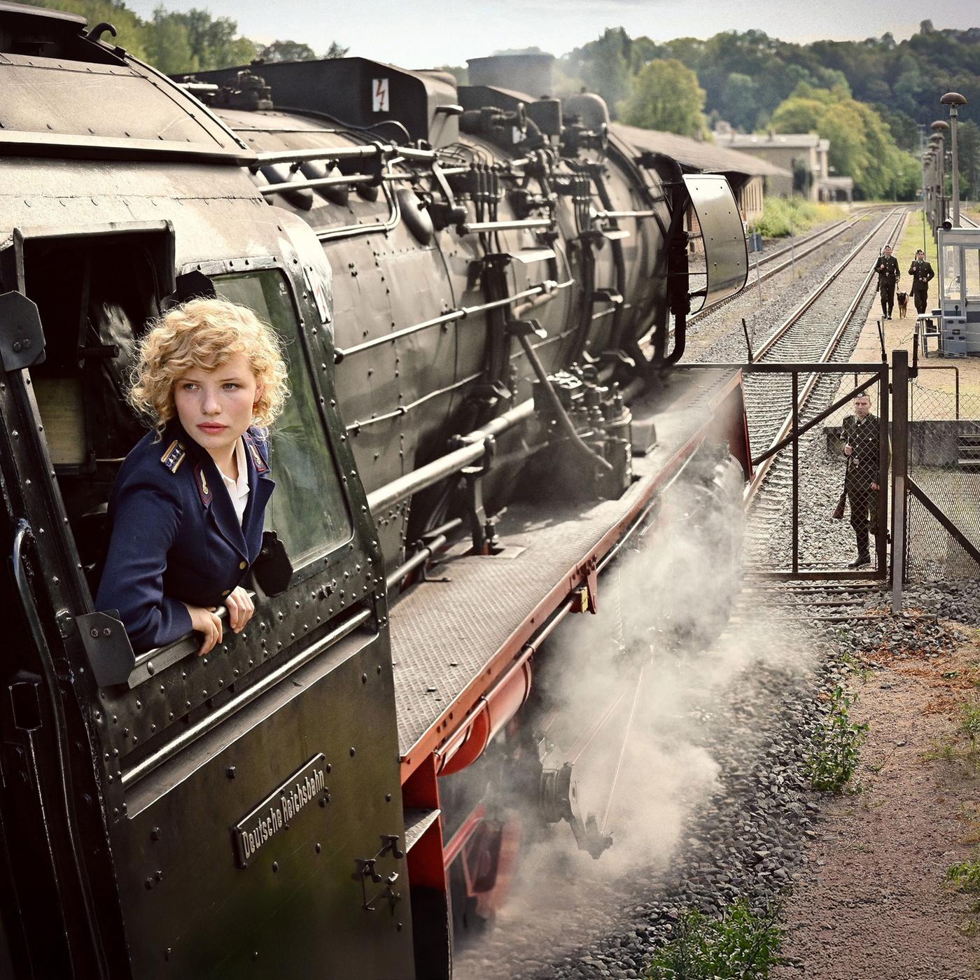 Eine blonde Frau streckt den Kopf aus einer Dampflokomotive