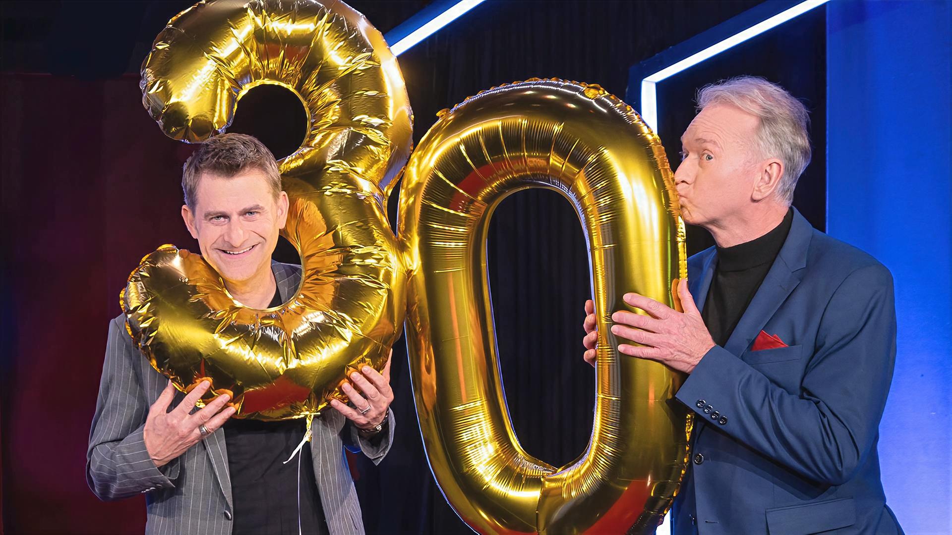 Michael Altinger (l.) und Christian Springer spielen mit goldenen Luftballons in der Form der Zahlen Drei und Null.