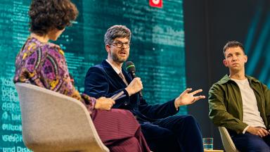Auf einer Bühne diskutieren zwei Männer und eine Frau.