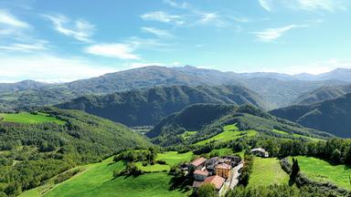 Luftaufnahme einer Berglandschaf und eines kleiner Hofes auf grünen Wiesen