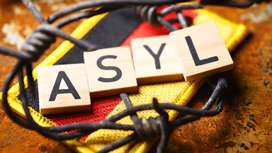 Das Wort Asyl liegt auf einer Deutschlandflagge. Rundherum ist Stacheldraht.