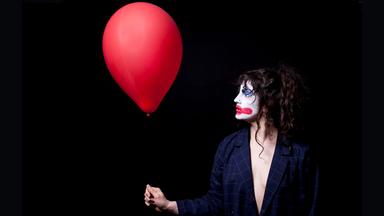 Frau mit geschminktem Clownsgesicht hält einen Luftballon.