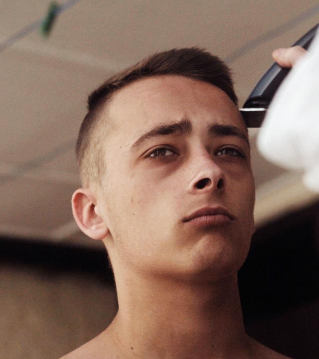 Junger Mann schaut genervt in die Gegend während er die Haare rasiert bekommt.