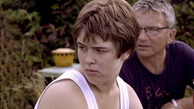 Eine junge Frau und ein bartloser Mann mit Brille sitzen zusammen auf einer Bank im Grünen und schauen in die Ferne