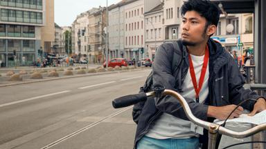 Junger Mann steht an einem Geländer und macht sich auf einem Blatt Papier Notizen.
