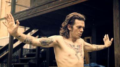 Ab 18! - Joe Boots - Tätowierter Mann mit ausgebreiteten Armen.