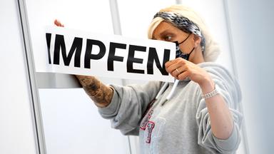 Frau entfernt den Schriftzug "Impfen" von einer Glastür beim Abbau eines Impfzentrums