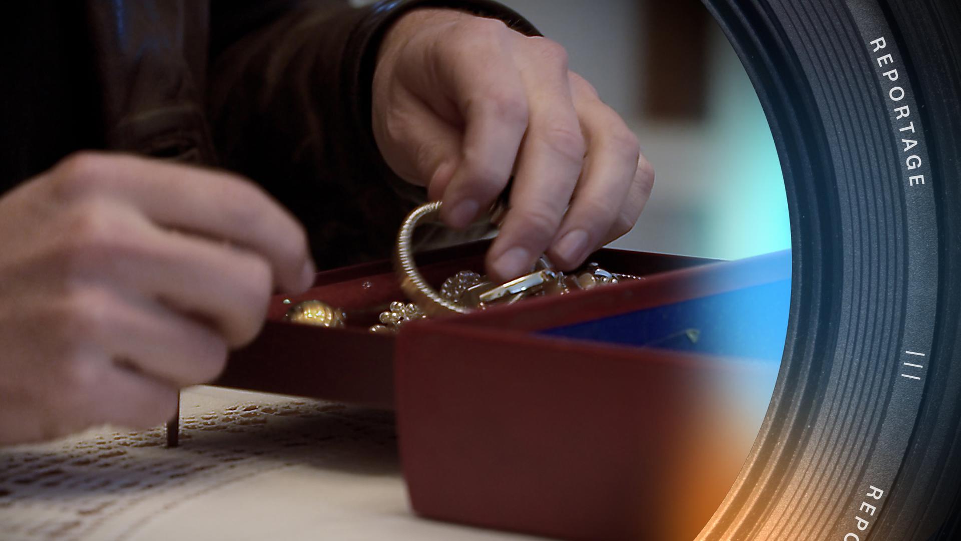 Nahaufnahme von Händen, die Goldschmuck aus einer Schmuckschatulle nehmen.