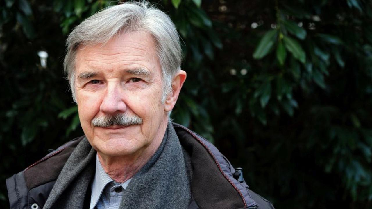 älterer Herr mit Hemd und Krawatte und Schnauzbart vor einer dunkleren Hecke. Portrait.