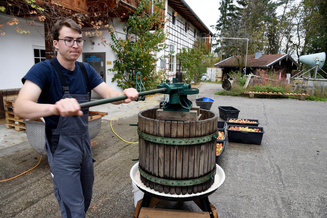 Ein junger Mann vor einem Haus arbeit an einer Apfelsaftpresse