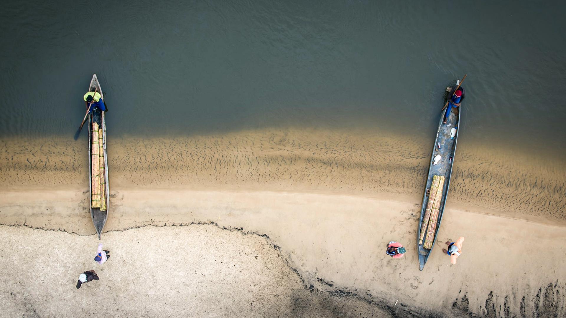 Blick von oben auf zwei längliche Boote am Ufer.