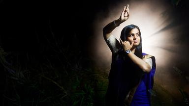 Sagitha macht eine Geste ihres traditionellen tamilischen Tanzes. Sie trägt einen traditionellen Sari.