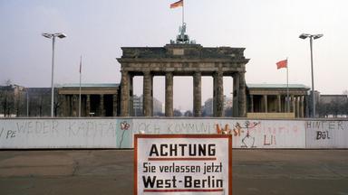 Blick auf das Brandenburger Tor hinter der Berliner Mauer. Im Vordergrund steht ein Schild mit der Aufschrift "Achtung! Sie verlassen jetzt West-Berlin".
