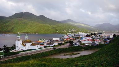 Blick auf den Ort Dutch Harbour auf Unlalaska zwischen grünen Bergen und blauem Wasser.