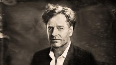 Schwarz-Weiß Bild eines Mannes mit lockigem Haar und Anzug