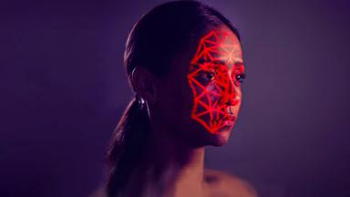 Eine Frau schaut ausdruckslos. Über ihr Gesicht ziehen sich netzartig rote Lichter, wie von einem Scanner.