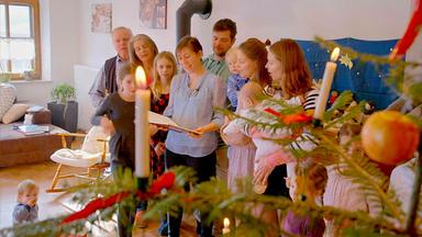 Eine große Familie singt vor einem Weihnachtsbaum.