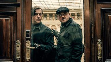 Zwei Männer blicken durch eine Glastür.