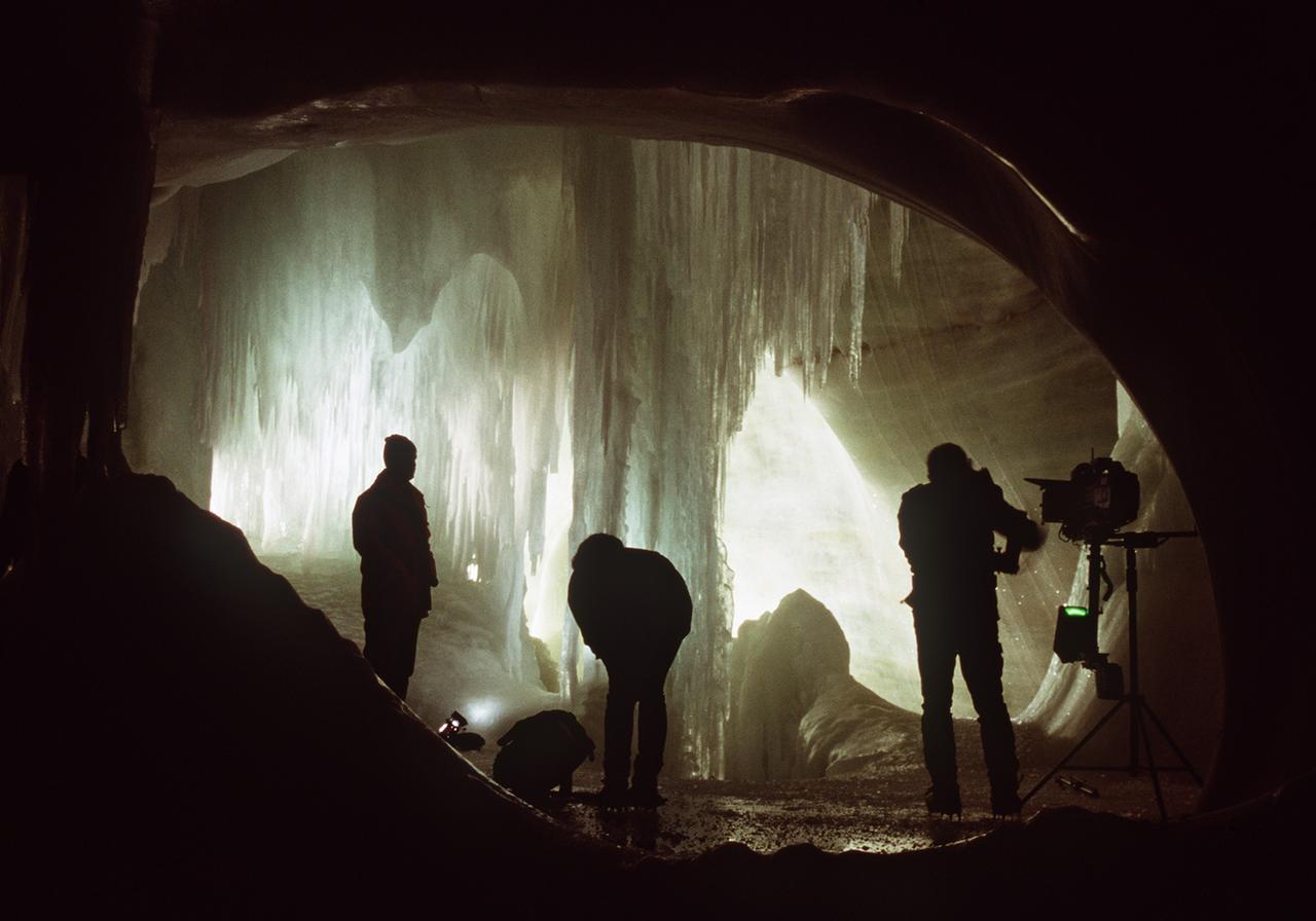 Drei Männer stehen in einer Eishöhle vor Eiszapfen
