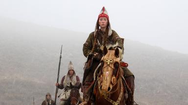 Stammesführerin Alkaya reitet auf ihrem Pferd voran. Berittene Soldaren mit Speeren folgen ihr in nebeliger Landschaft.