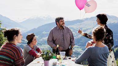 Mann umringt von Angehörigen auf Bergterrasse bekommt Luftballons