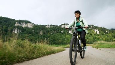 Andrea Ballschuh fährt auf einem Fahrrad durch eine grüne Landschaft, sie trägt einen Helm.