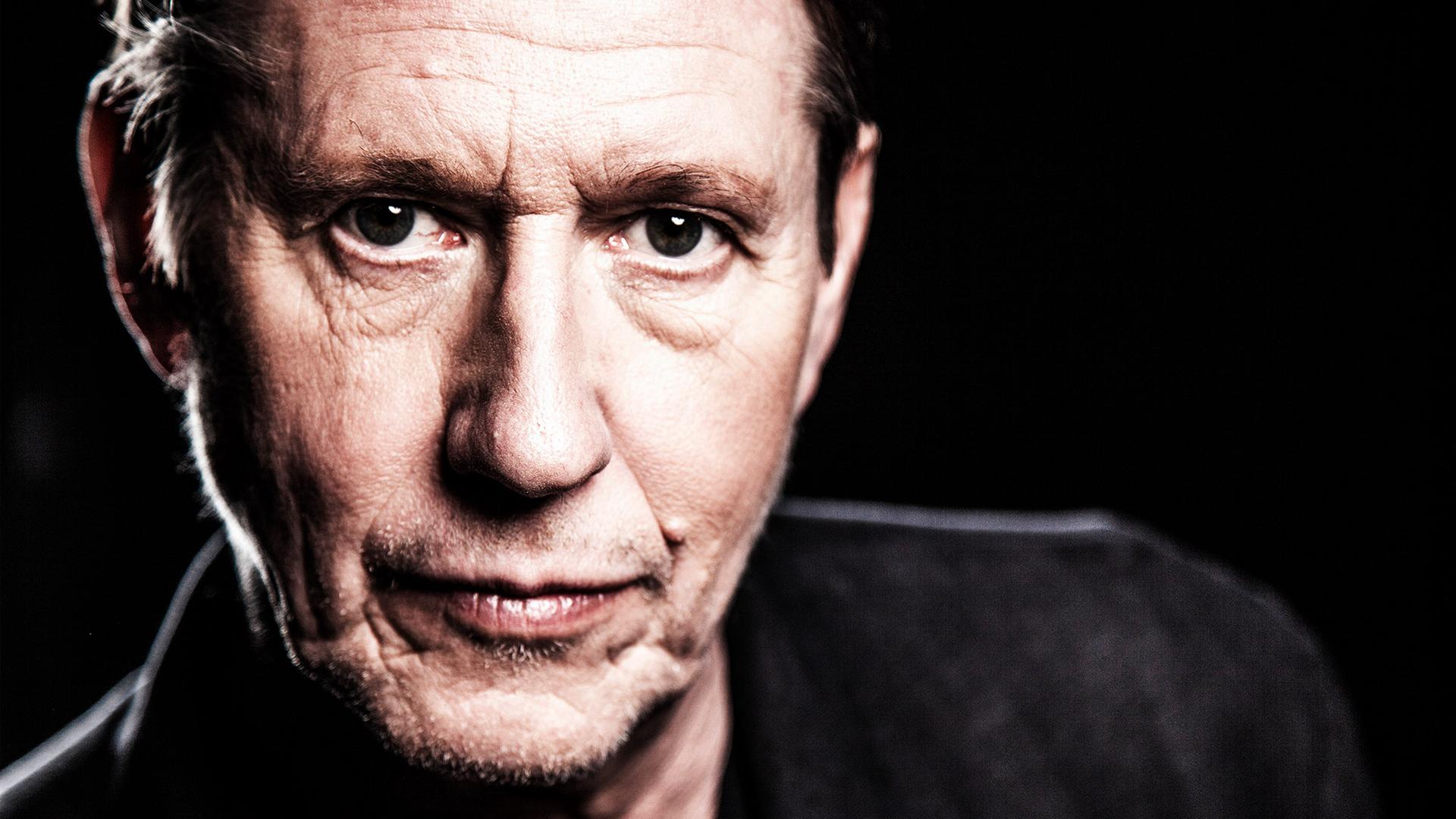 Ein Mann blickt vor schwarzem Hintergrund in die Kamera.