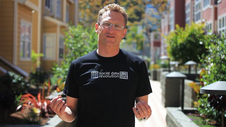 Andreas Weigend steht kleinen Straße zwischen bunten Häusern. Mit den Händen gestikuliert er.