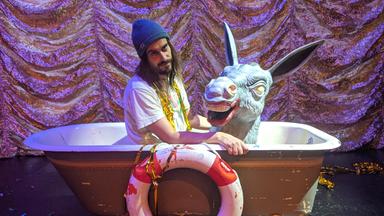 Ein Mann mit Strickmütze sitzt mit einer Eselsfigur in einer Badewanne. An die Badewanne ist ein Rettungsring gebunden.