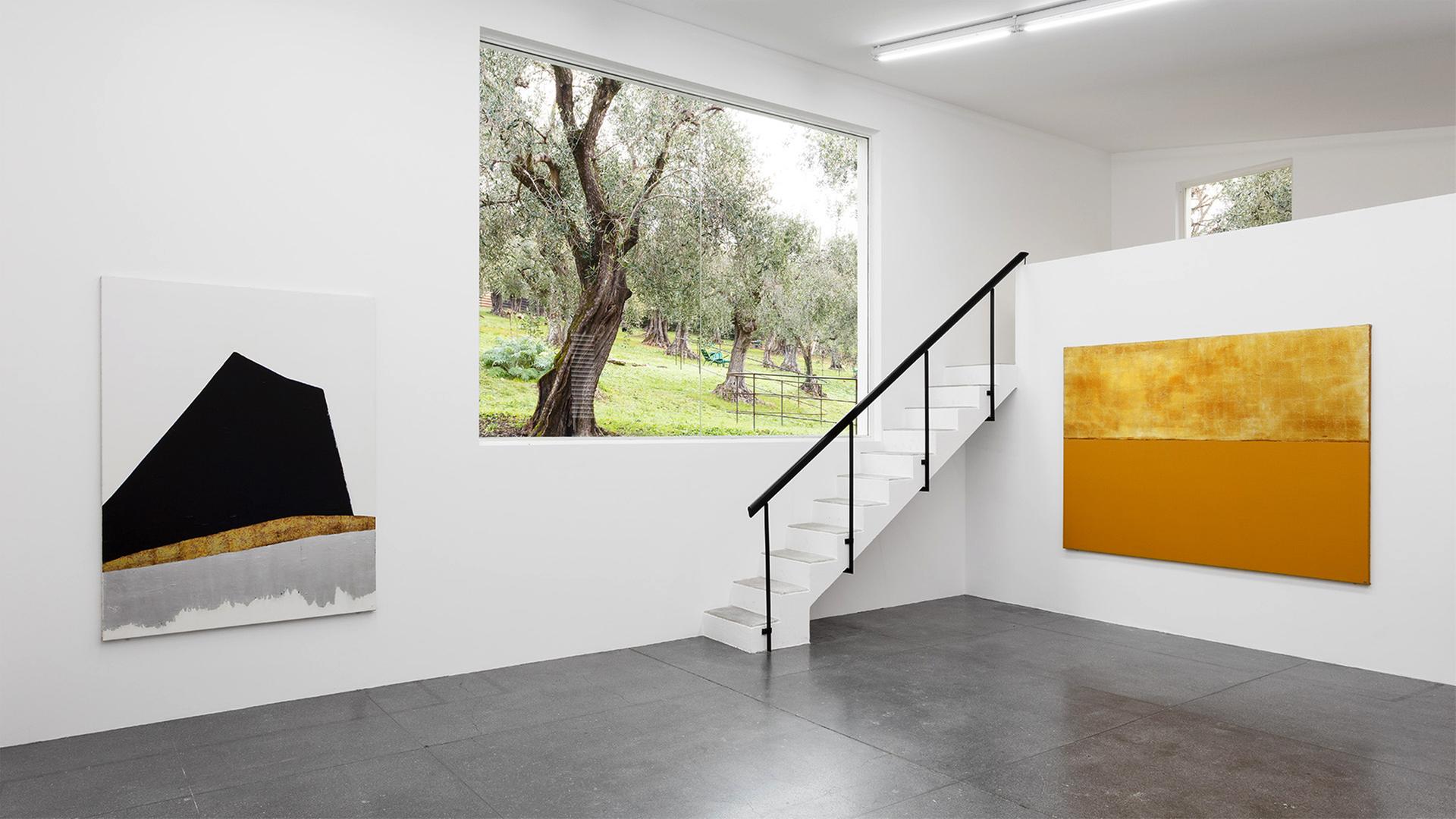 Ein heller Raum mit weißen Wänden, an denen Malereien hängen.