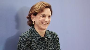 Porträtfoto einer Frau mittleren Alters mit kurzen lockigen braunen Haaren, die in die Kamera lächelt.