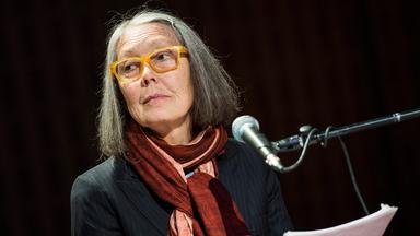 Porträtfoto einer älteren Frau mit schulterlangen grauen Haaren und einer Brille mit gelbem Kunststoffrahmen.